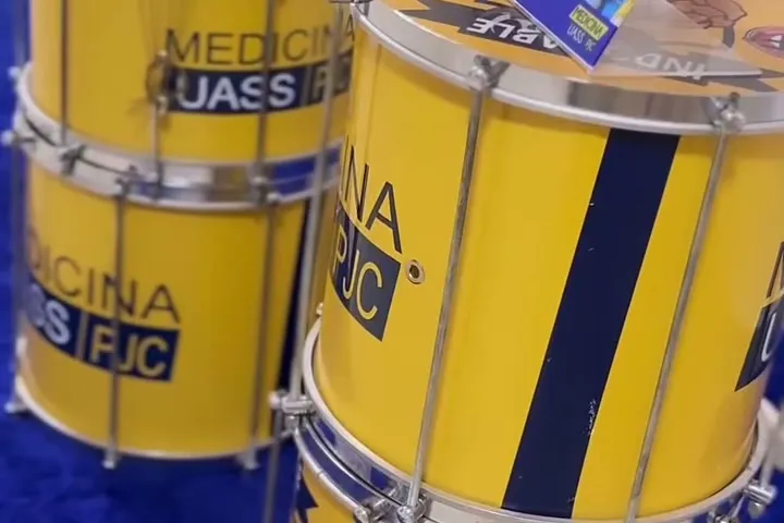 Tambores da bateria da Atlética, pintados de amarelo e azul com a marca Medicina UASS/PJC