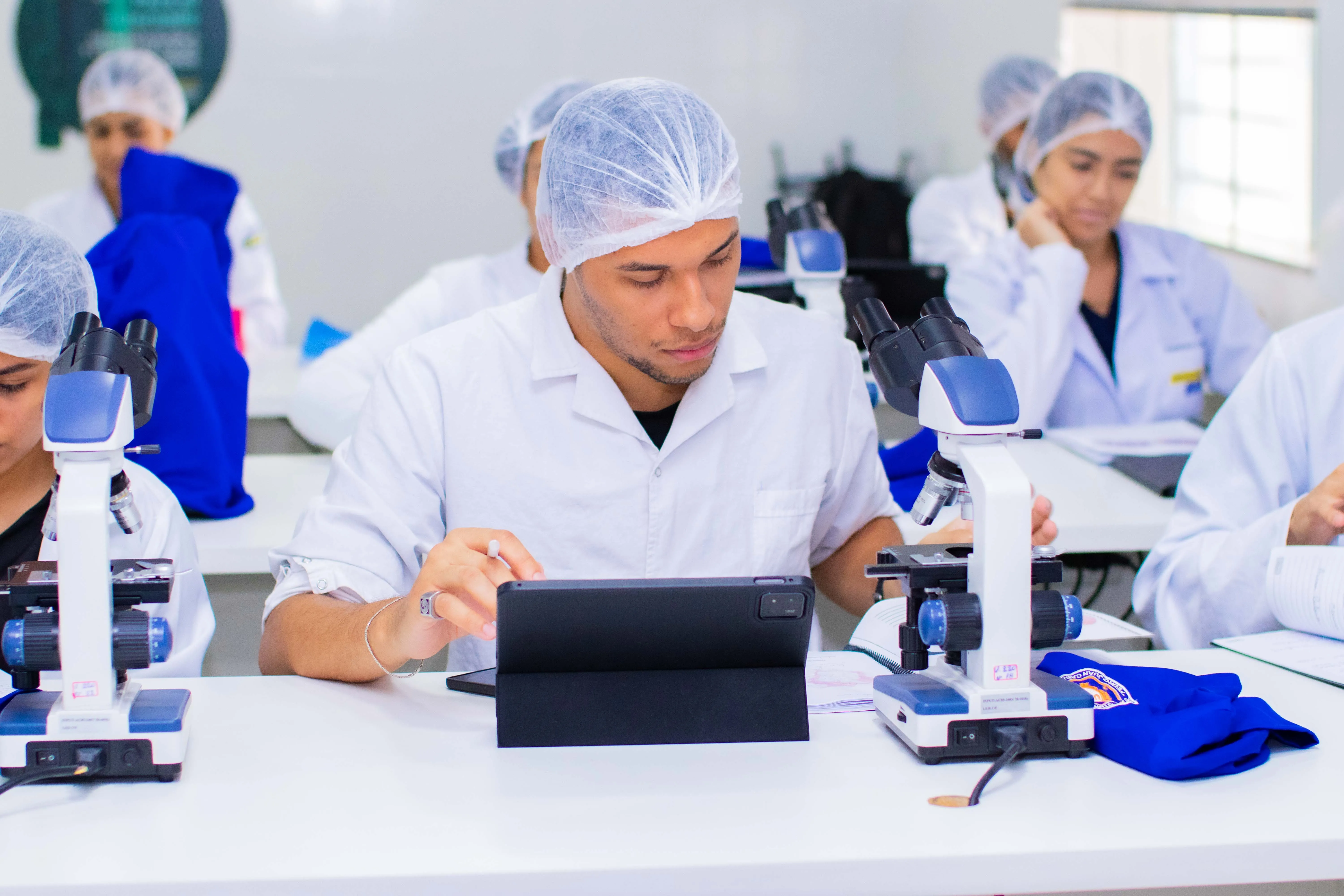 Aula de laboratório com estudantes em bancada de microscópios na UASS-PJC