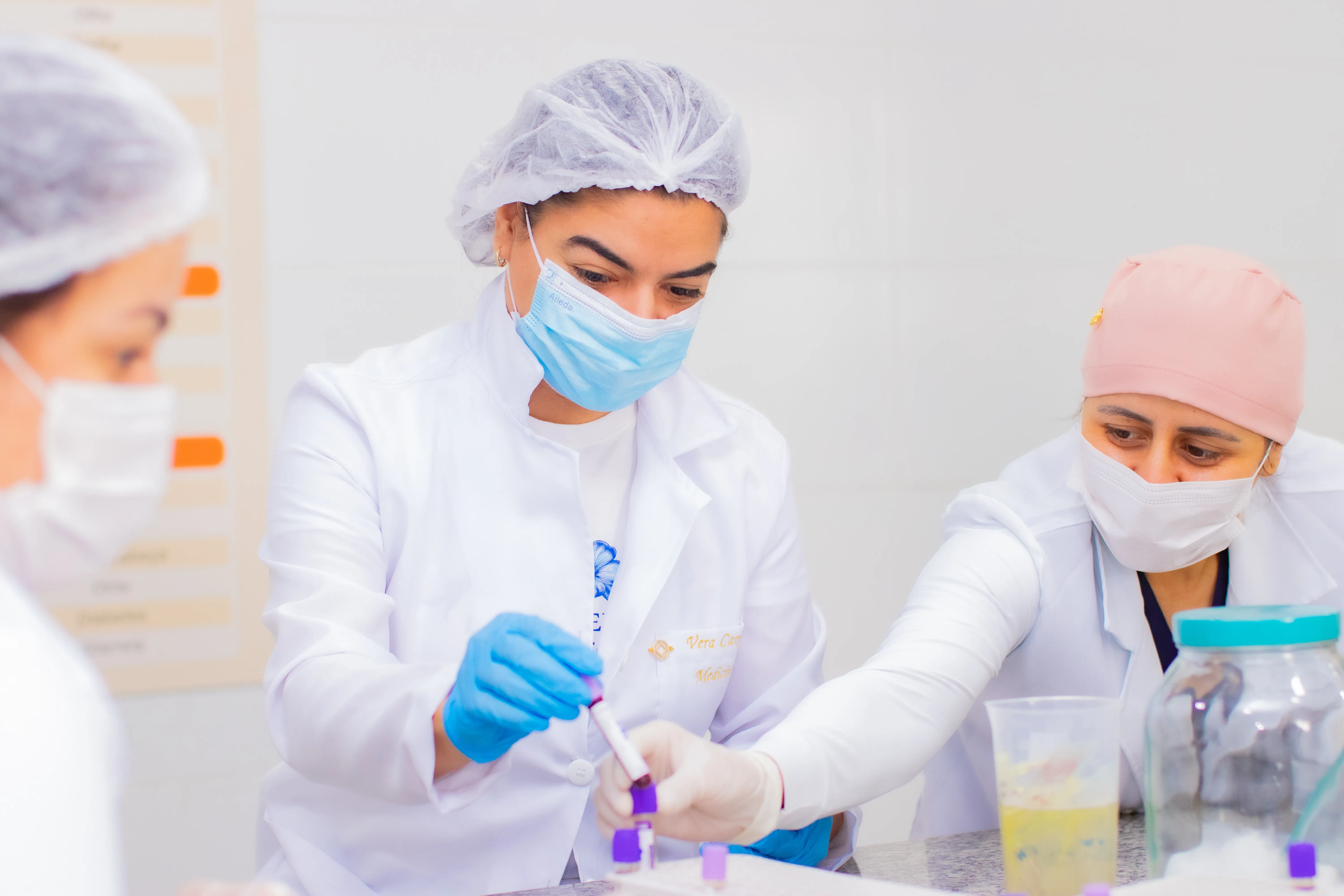 Alunas de jaleco e touca manipulando amostras no laboratório