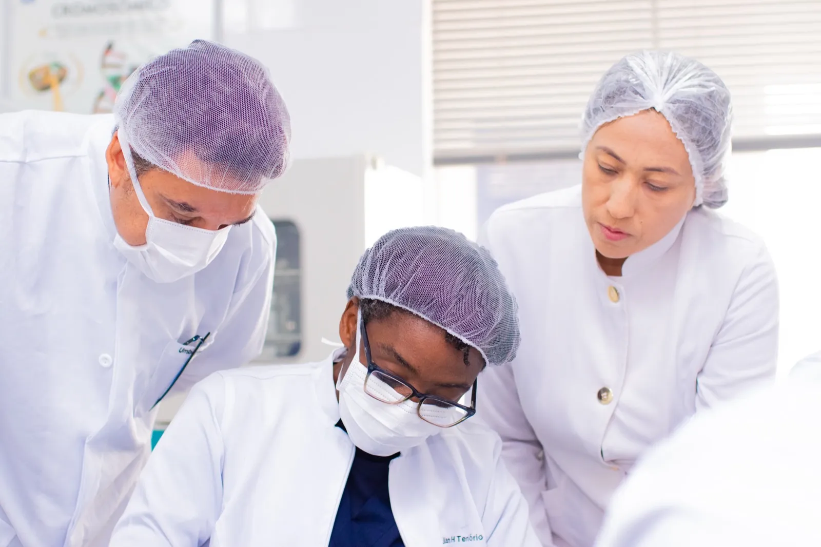 Professor orientando duas estudantes de Medicina durante atividade de laboratório