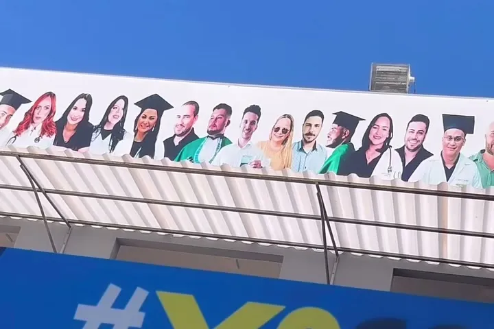 Painel na fachada da faculdade com fotos de formandos de beca e jaleco