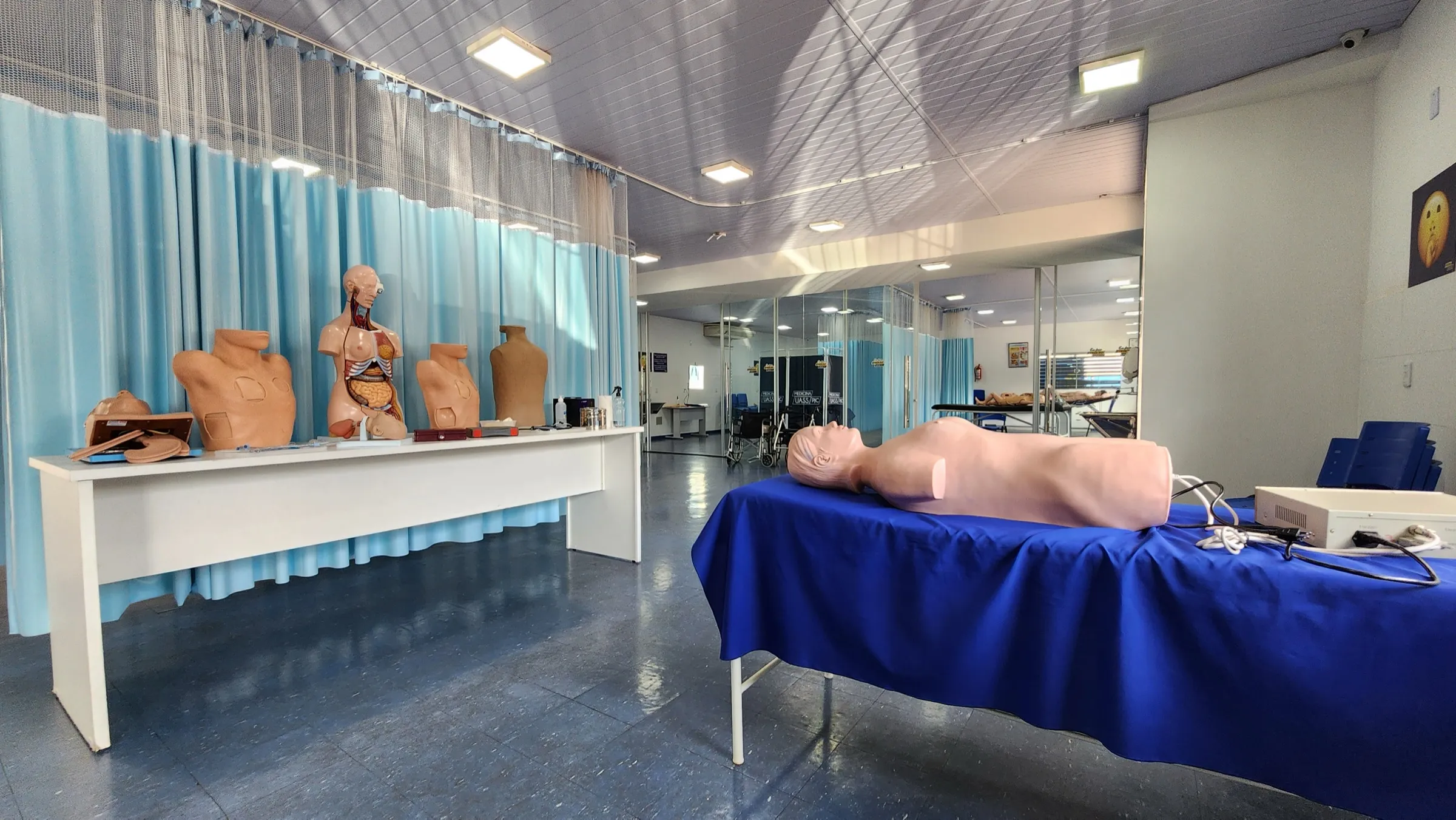 Sala de simulación de la UASS-PJC con un simulador de torso sobre la camilla azul y bustos anatómicos en la mesada del fondo