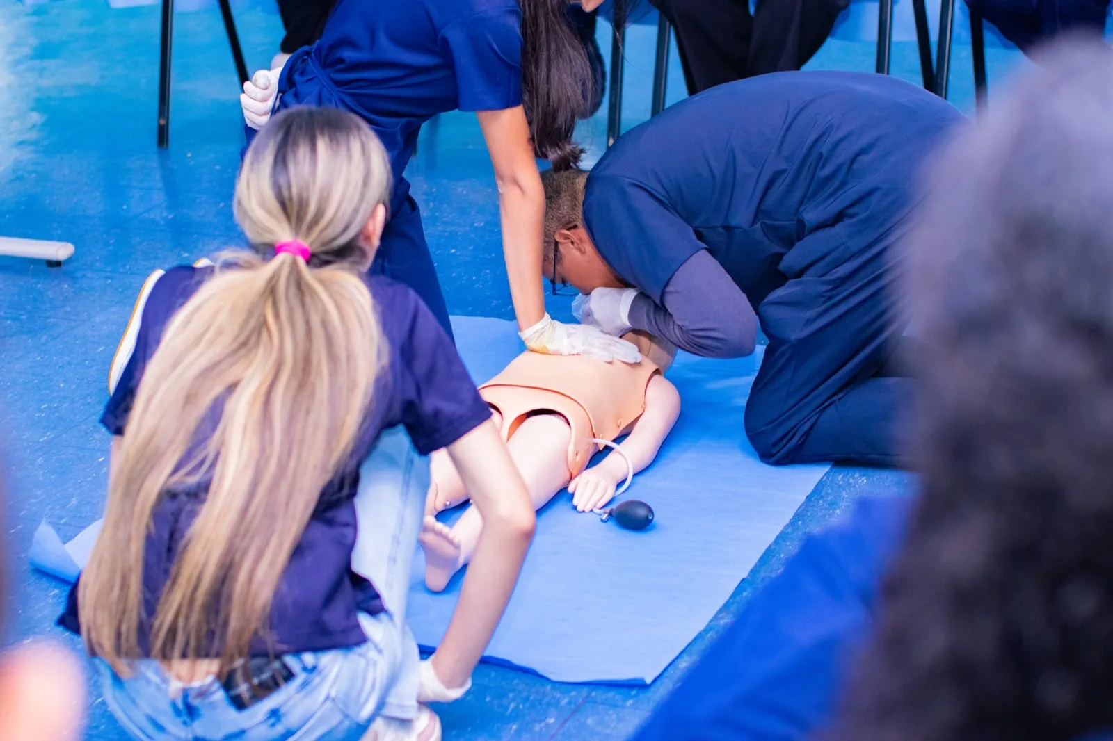 Estudantes de Medicina em treinamento de atendimento de emergência, trabalhando em equipe ao redor de um manequim de simulação